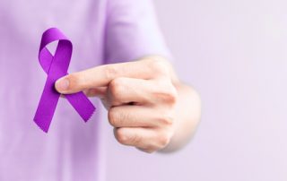 Mão segurando um laço lilás da campanha contra o câncer de útero