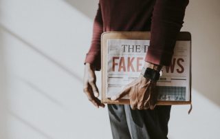 Homem segurando um jornal com Fake News nele.