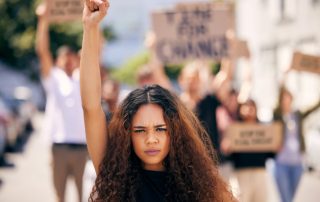 Uma mulher jovem de cabelos cacheados com punho ao alto simbolizando a luta do Dia Internacional das Mulheres